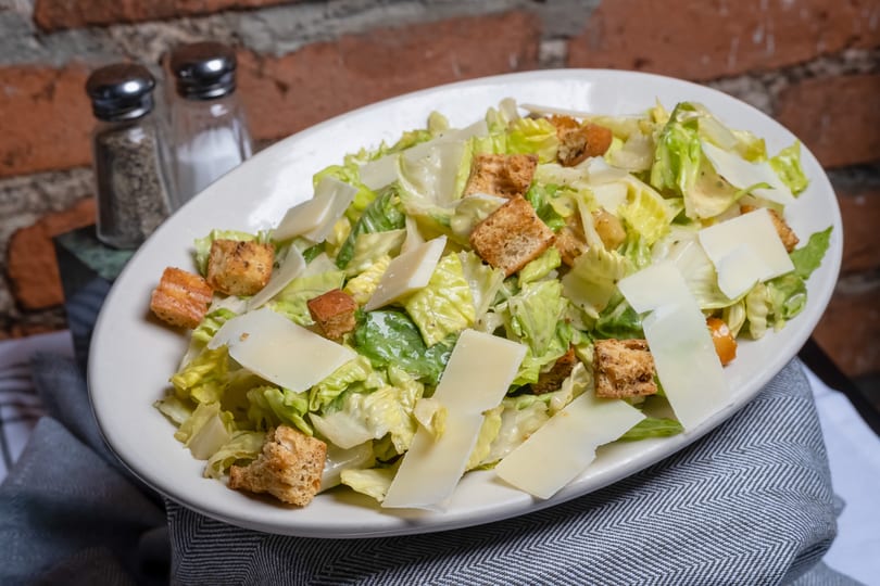 Classic Caesar salad with crisp romaine, golden croutons, and shaved Parmesan on a white plate.