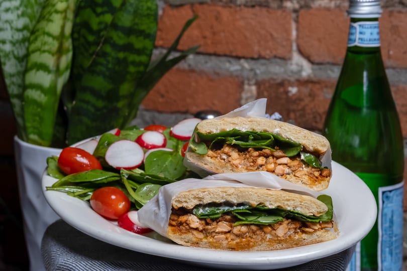 Chicken sandwich halves with spinach and a side salad with tomatoes and radishes, by a green bottle.