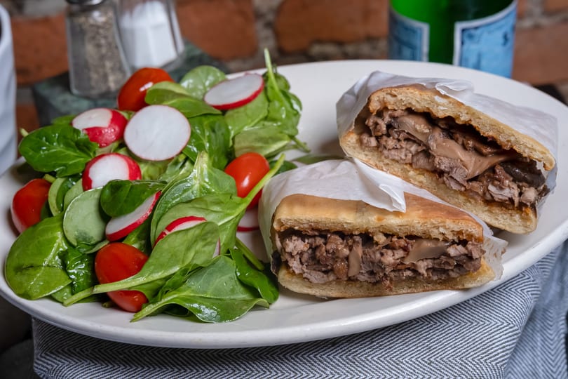 A hearty meat and mushroom sandwich, cut in half, served with a fresh spinach and radish salad.