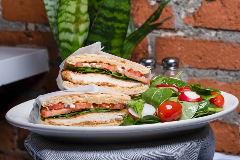 Crispy chicken sandwich halves with lettuce, tomato, and sauce, served with a fresh green salad.